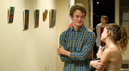 SIUE senior Sutton Allen visits with an attendee during his exhibit at the Youth Education and Health in Soulard. His paintings are displayed in the background.