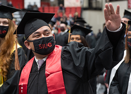 An SIUE graduate waves to his supporters during a commencement ceremony in the Vadalabene Center First Community Arena.