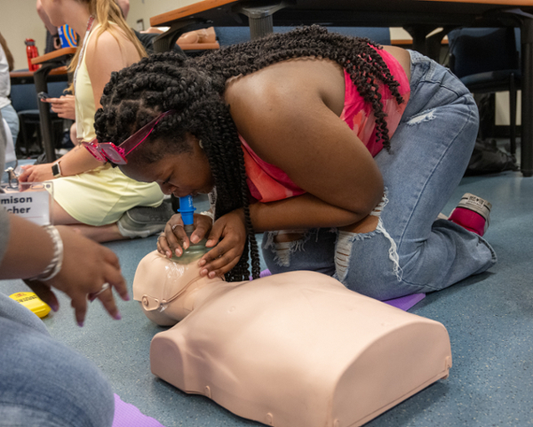 Student bending over model and administering CPR