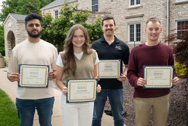 Four SIUE SDM students hold framed plaques of their awards