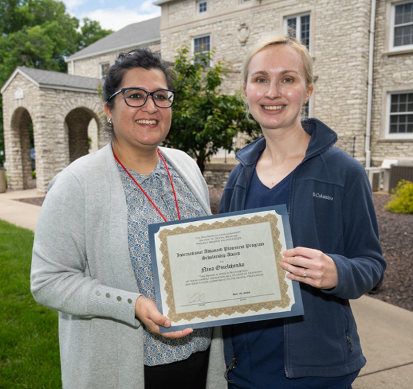 SIU SDM third year student Nina Omelchenko standing with her team member and holding her award